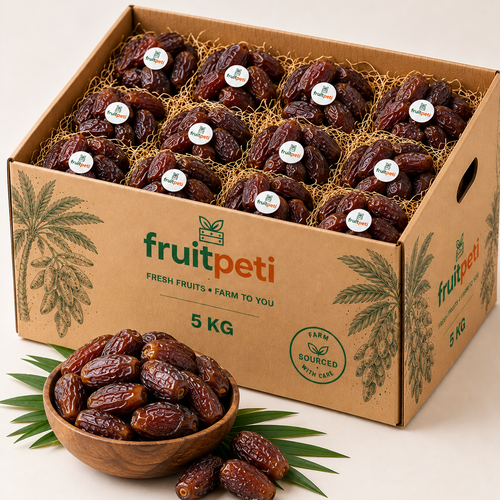 A 5 kg cardboard box of FruitPeti dates filled with individually wrapped dates, with a wooden bowl of loose dates and green palm leaves in the foreground on a light beige background.