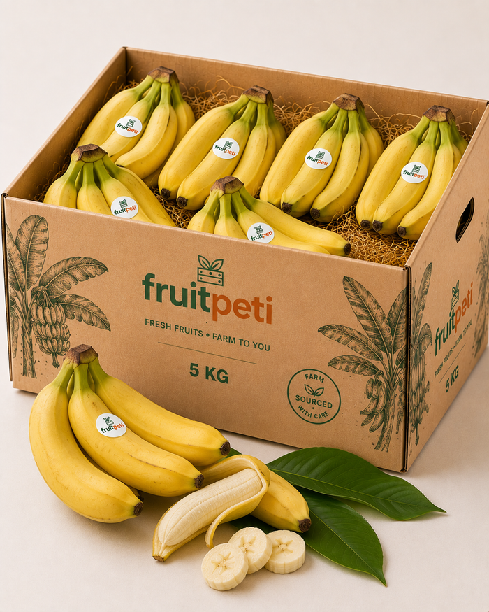 A 5 kg cardboard box of FruitPeti bananas, shown open with multiple bunches of yellow bananas inside. Additional loose bananas, a peeled banana, sliced bananas, and green leaves are arranged in front of the box on a clean white background.
